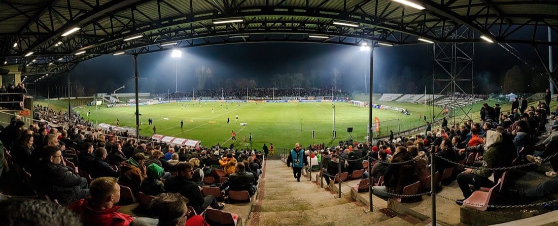 Floodlit football stadium at night, packed stands, glowing pitch